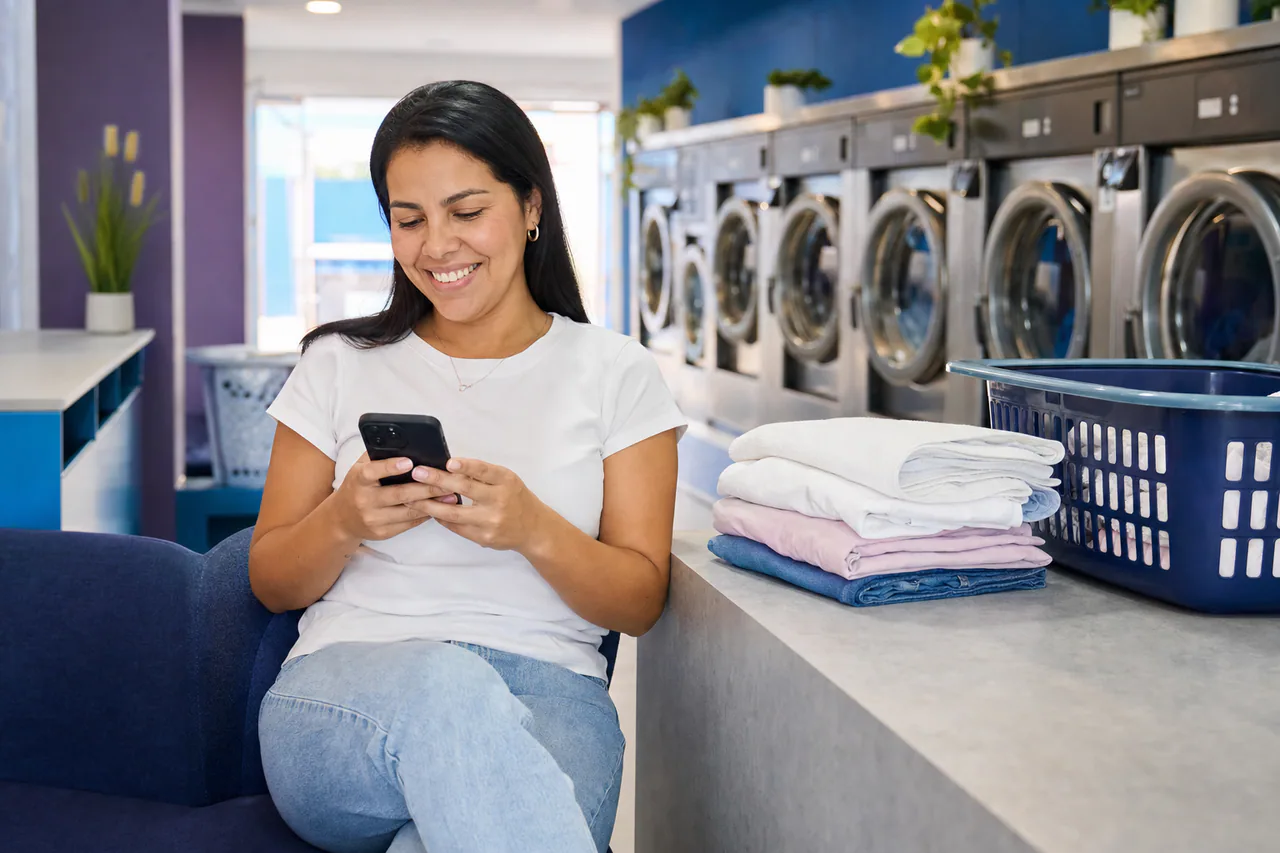 Cliente feliz usando o celular enquanto aguarda suas roupas